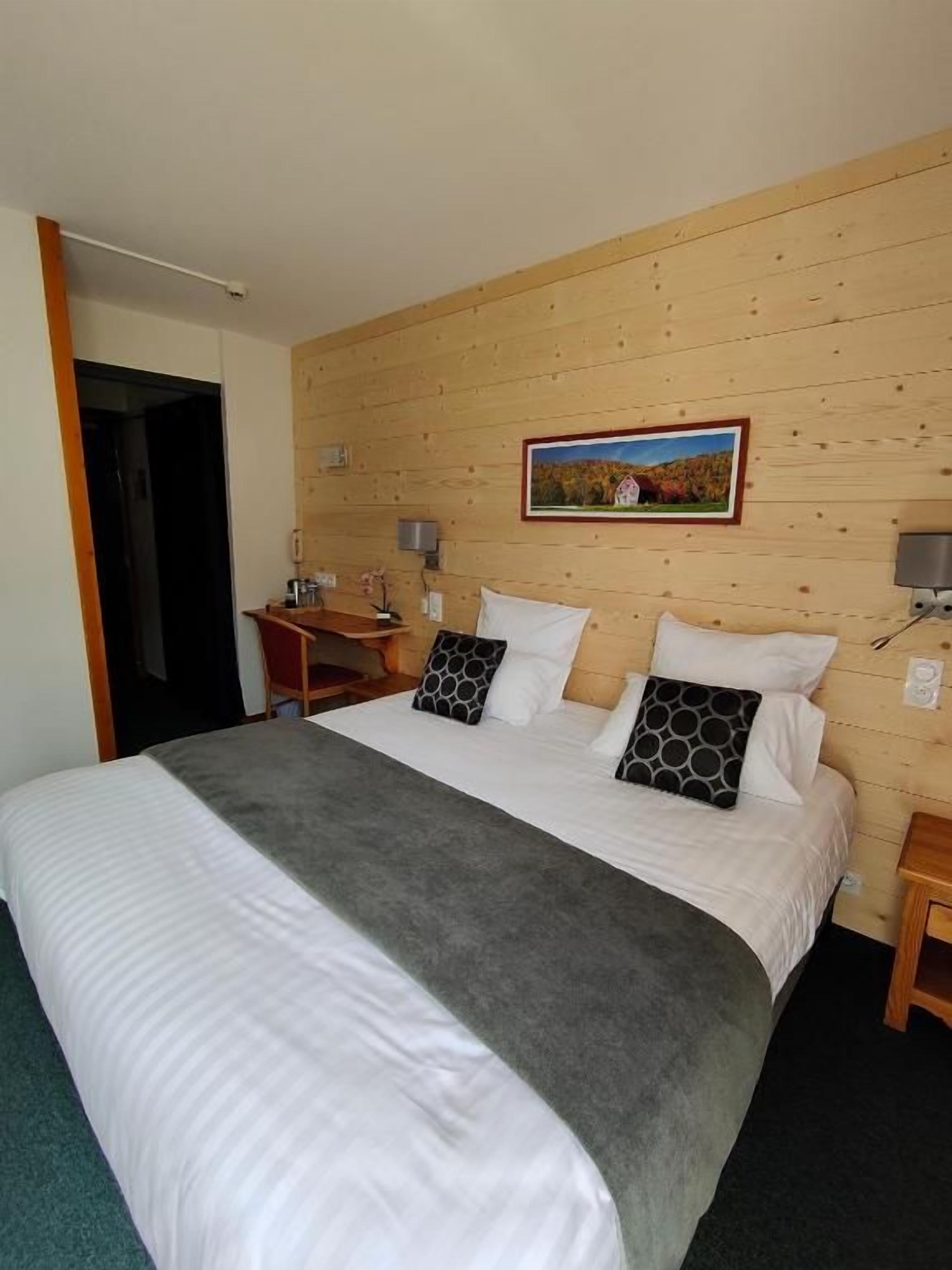 Habitación de hotel con pared de madera, una cama con ropa blanca, dos mesitas de noche y un cuadro enmarcado sobre la cama.