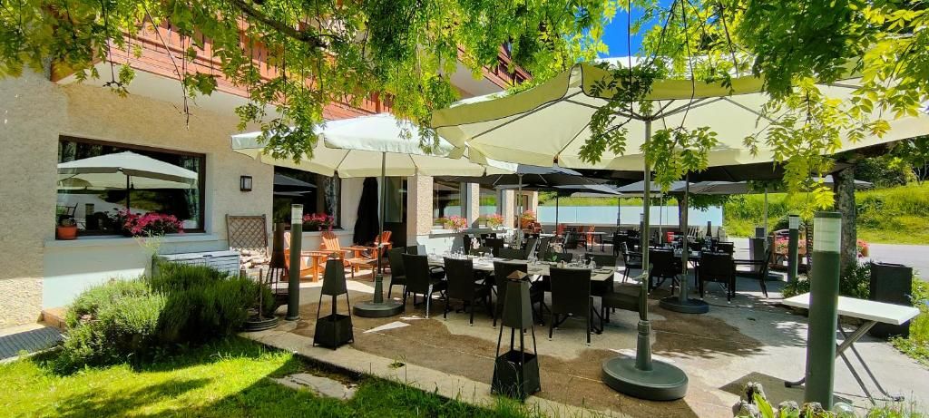 Un área de comedor al aire libre con mesas y sombrillas, rodeada de vegetación y una fachada de edificio.