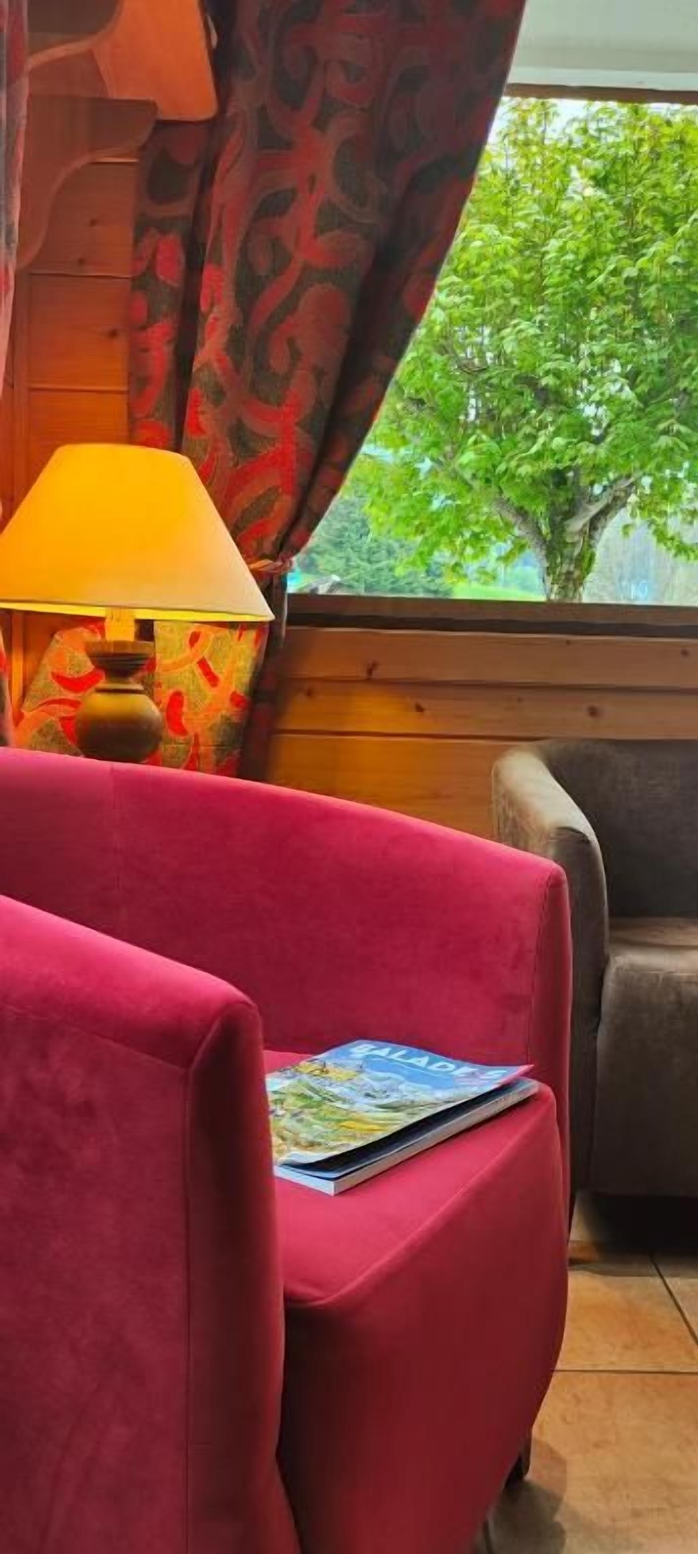 A room with a red chair, a lamp, and a window with curtains.