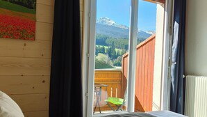 A bedroom with a bed, a view of a wooden deck, and a painting on the wall.