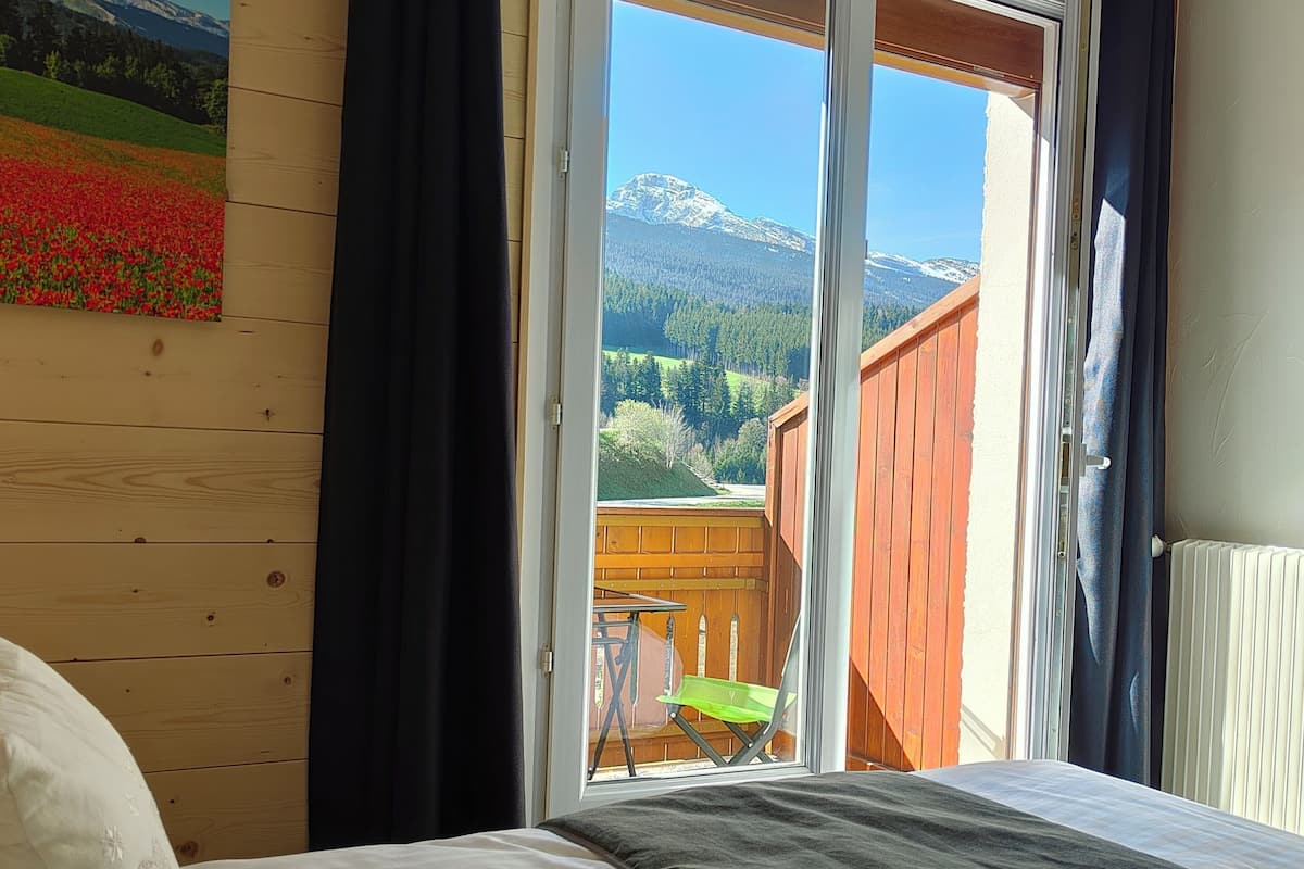 Ein Schlafzimmer mit Bett, Blick auf eine Holzterrasse und einem Bild an der Wand.