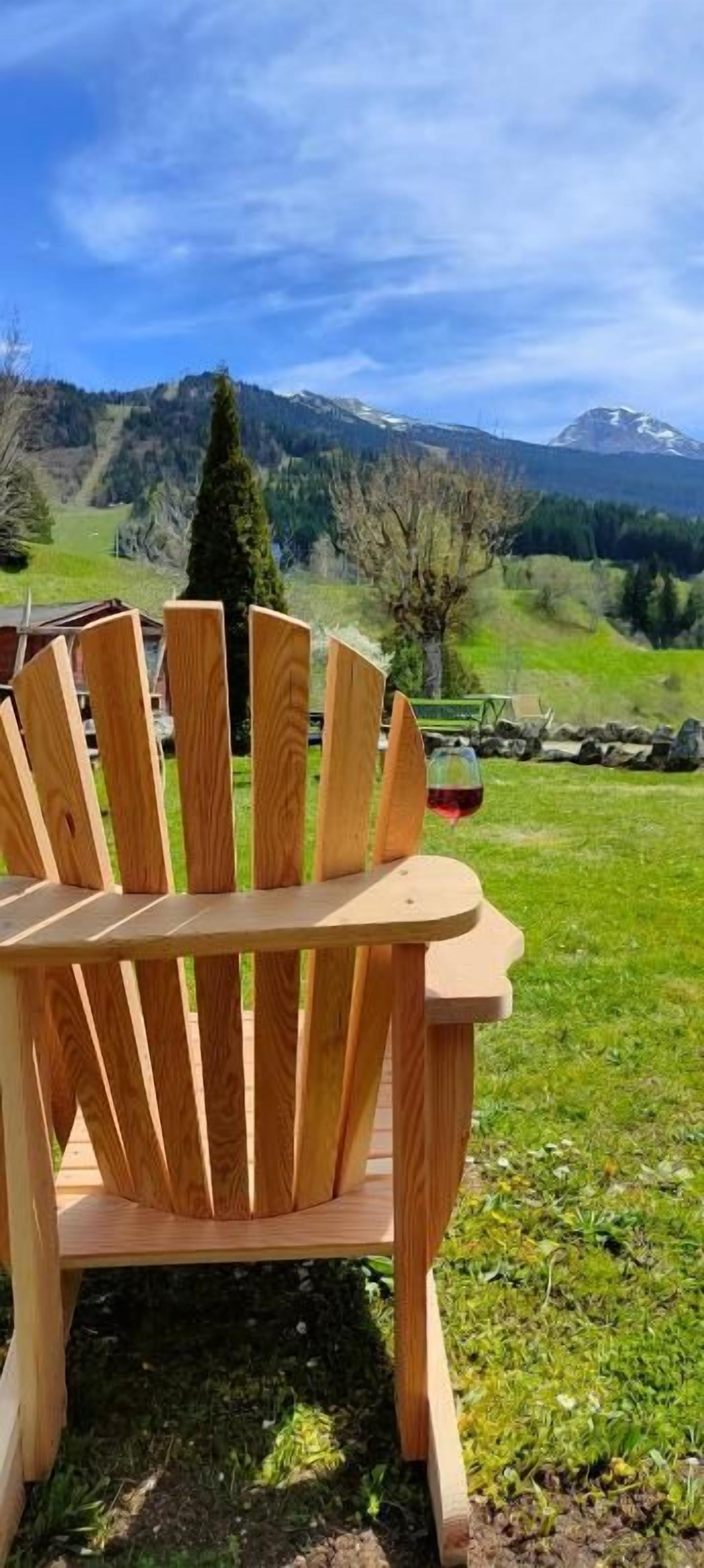 A wooden Adirondack chair outdoors with a mountainous landscape in the background.