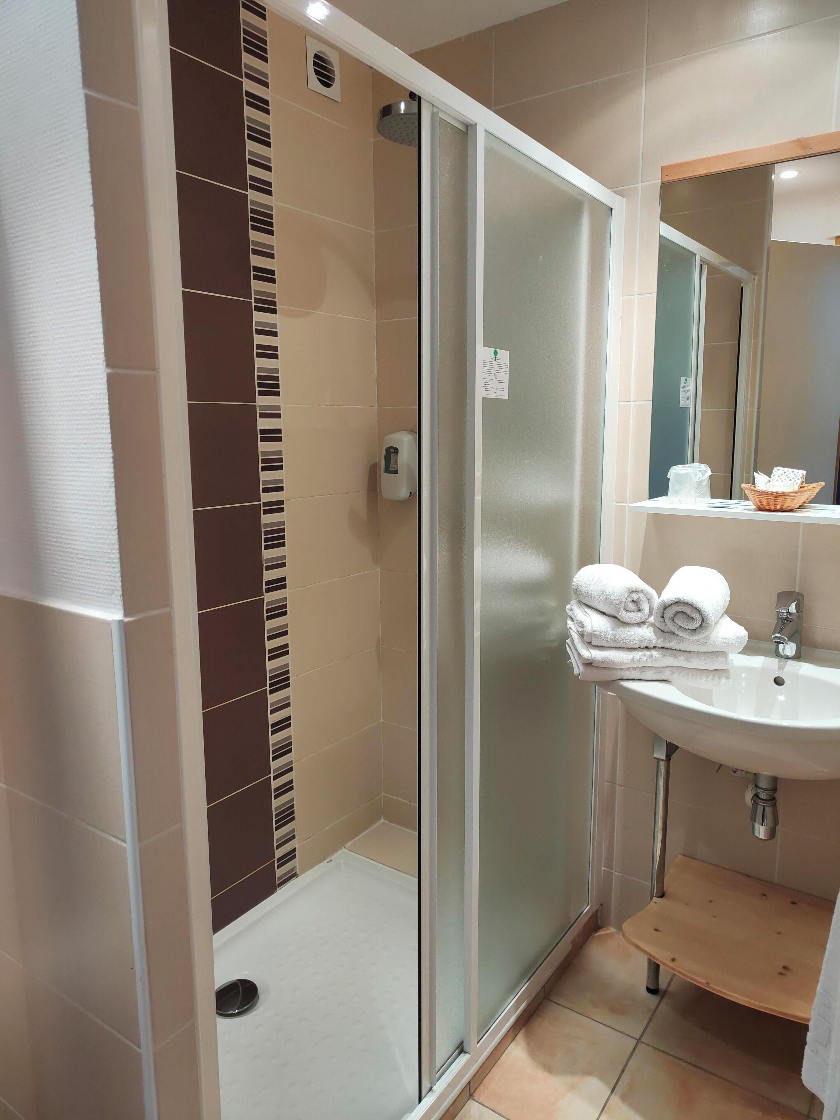 Ein modernes Badezimmer mit Duschkabine aus Glas, Waschbecken mit Spiegel und einer kleinen Holzbank.