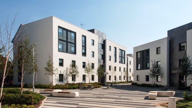 A modern building with a flat roof, large windows, and a paved area with benches. - Petros Court (Canterbury)