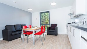 A modern kitchen with white cabinets, a dining area with red chairs, and a black sofa. - Petros Court (Canterbury)