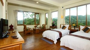 A hotel room with two beds, a TV, wooden furniture, and large windows offering a mountain view.
