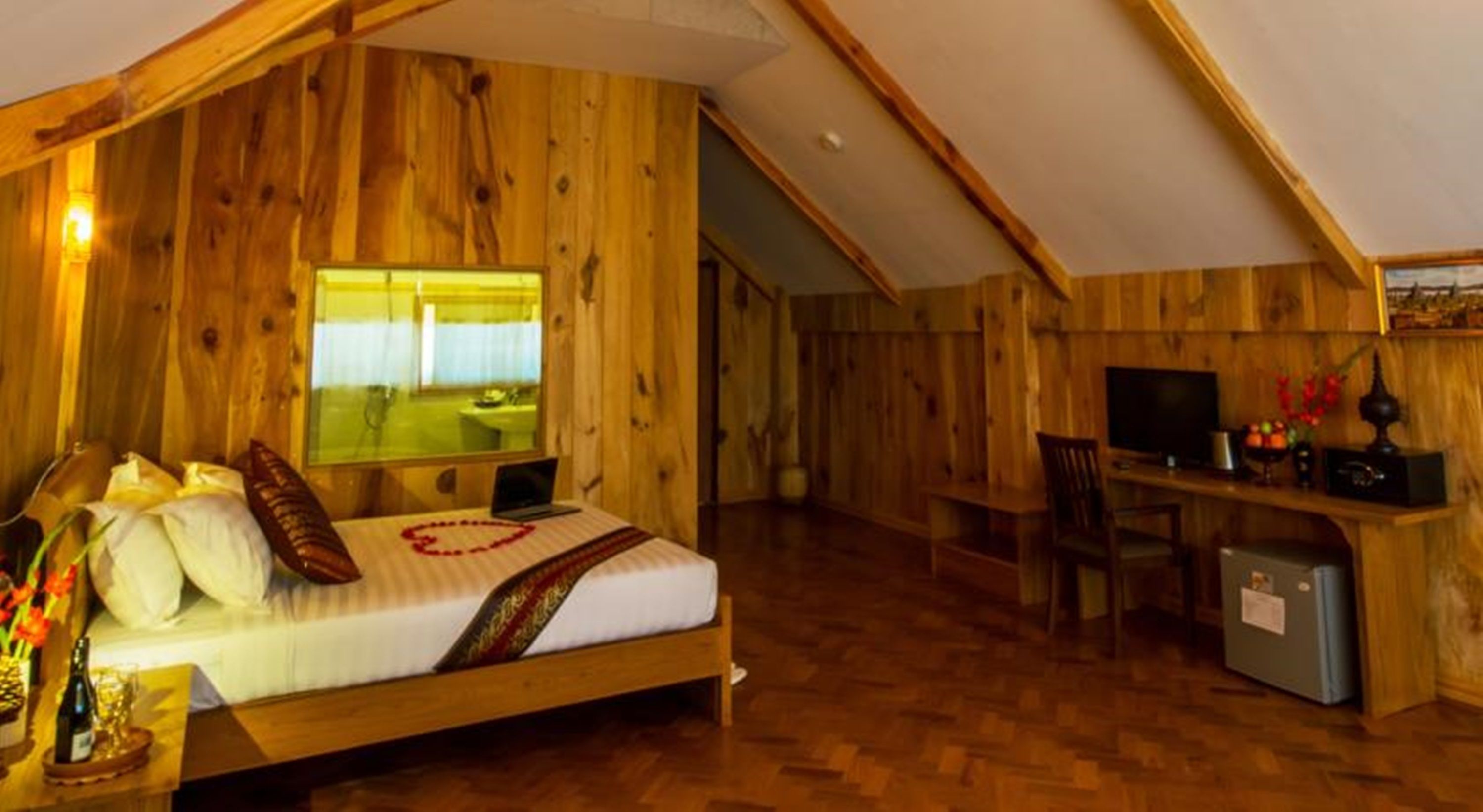 A cozy wooden room with a bed, a desk, and a television.