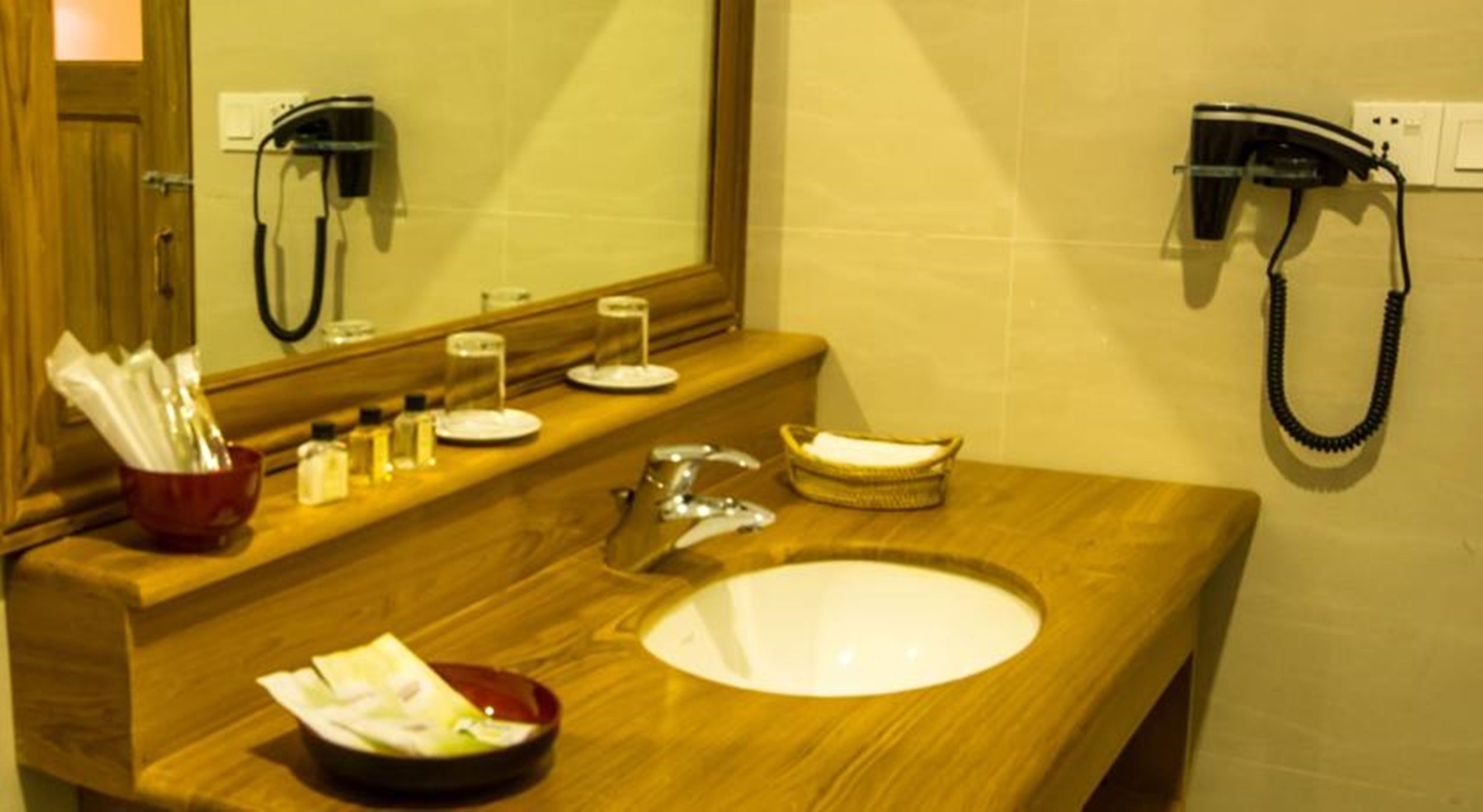 A bathroom with a wooden vanity, a sink, a mirror, a hairdryer, and a towel rack.