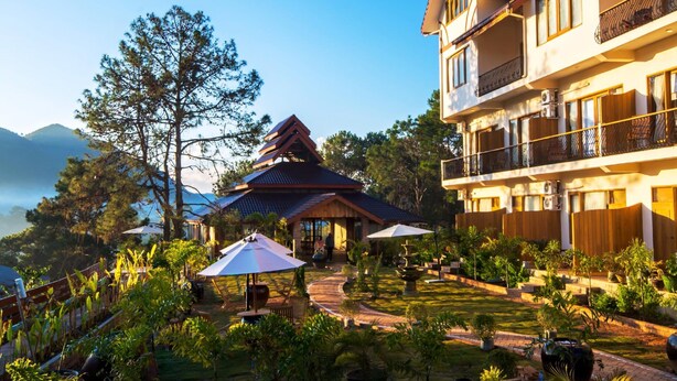 A hotel with a traditional pagoda-style building, a garden with various plants, and a pool area.