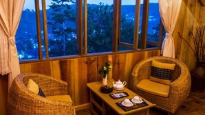 A cozy room with wicker furniture, a small table with tea set, and a view of a forested area through large windows.