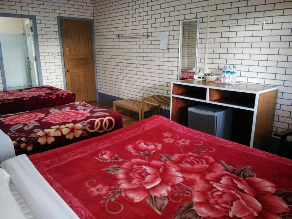 Una habitación con dos camas, una puerta de madera, un espejo, un tocador con lavabo y un pequeño taburete.