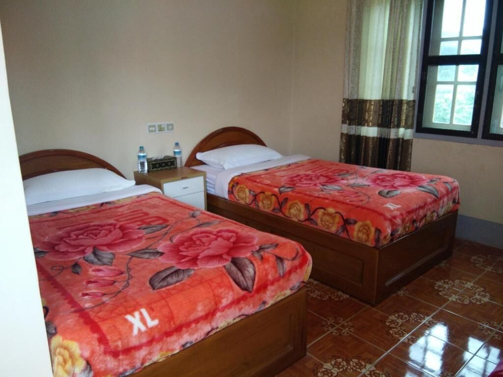 Une chambre avec deux lits, chacun agrémenté de draps à motifs floraux, une table de chevet avec une bouteille d’eau et une fenêtre avec des rideaux.