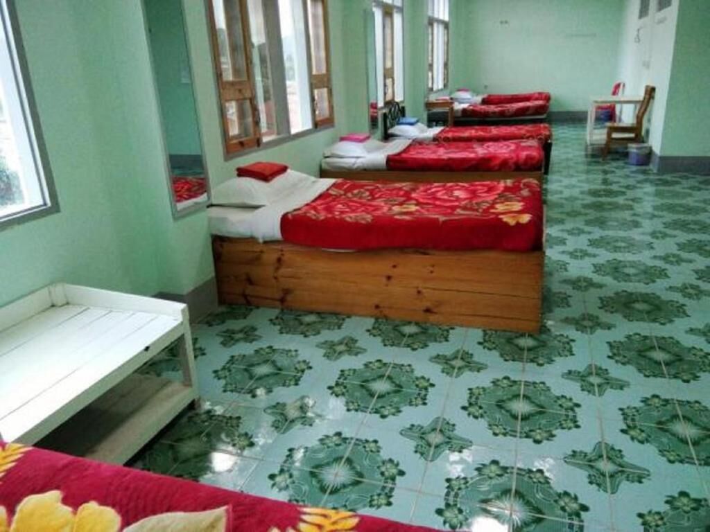 A room with multiple beds, each with red bedding, wooden headboards, and a green patterned floor.