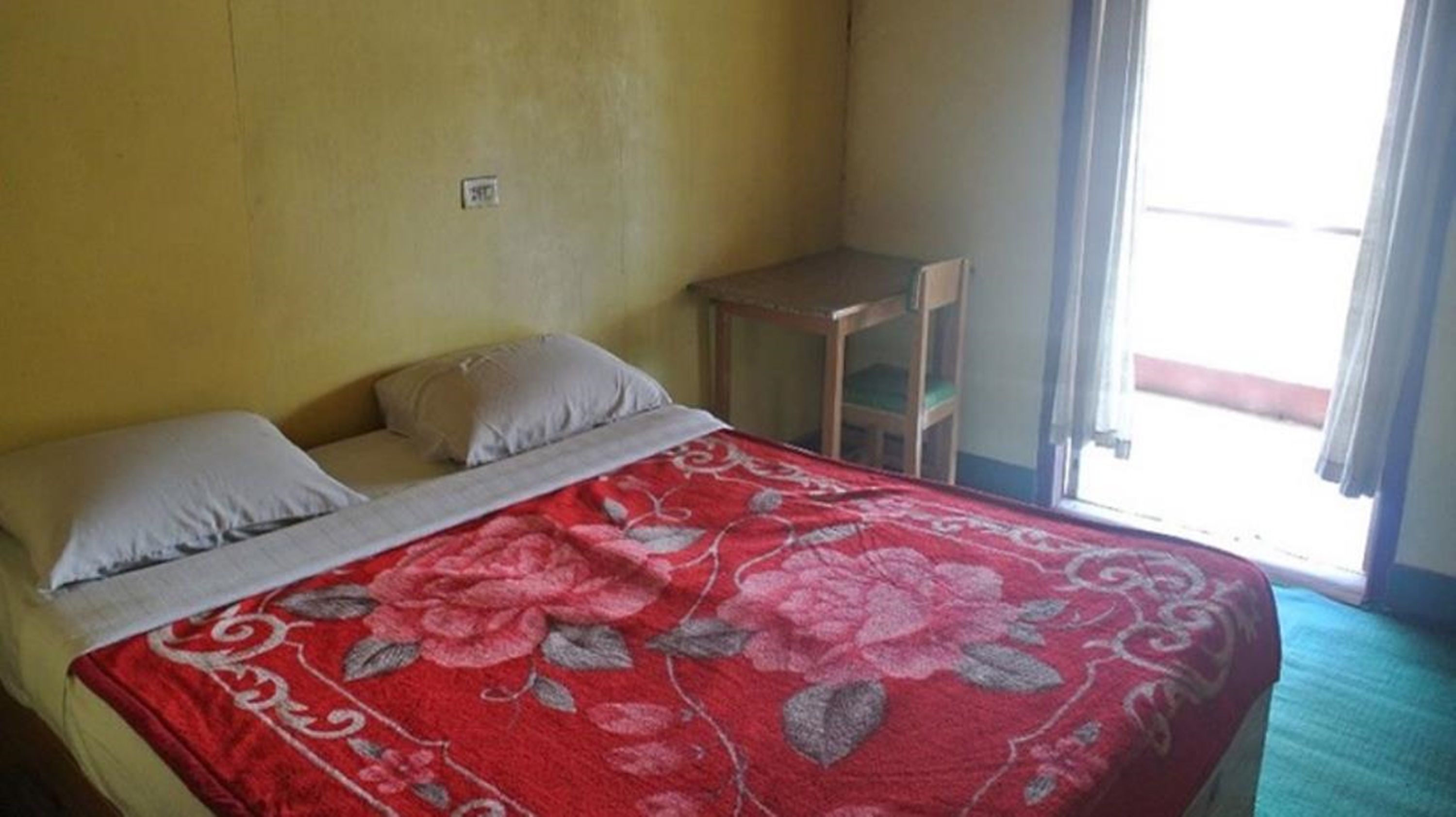 Ein Einzelbett mit floralem Überwurf, ein Nachttisch und ein Fenster mit Vorhängen.
