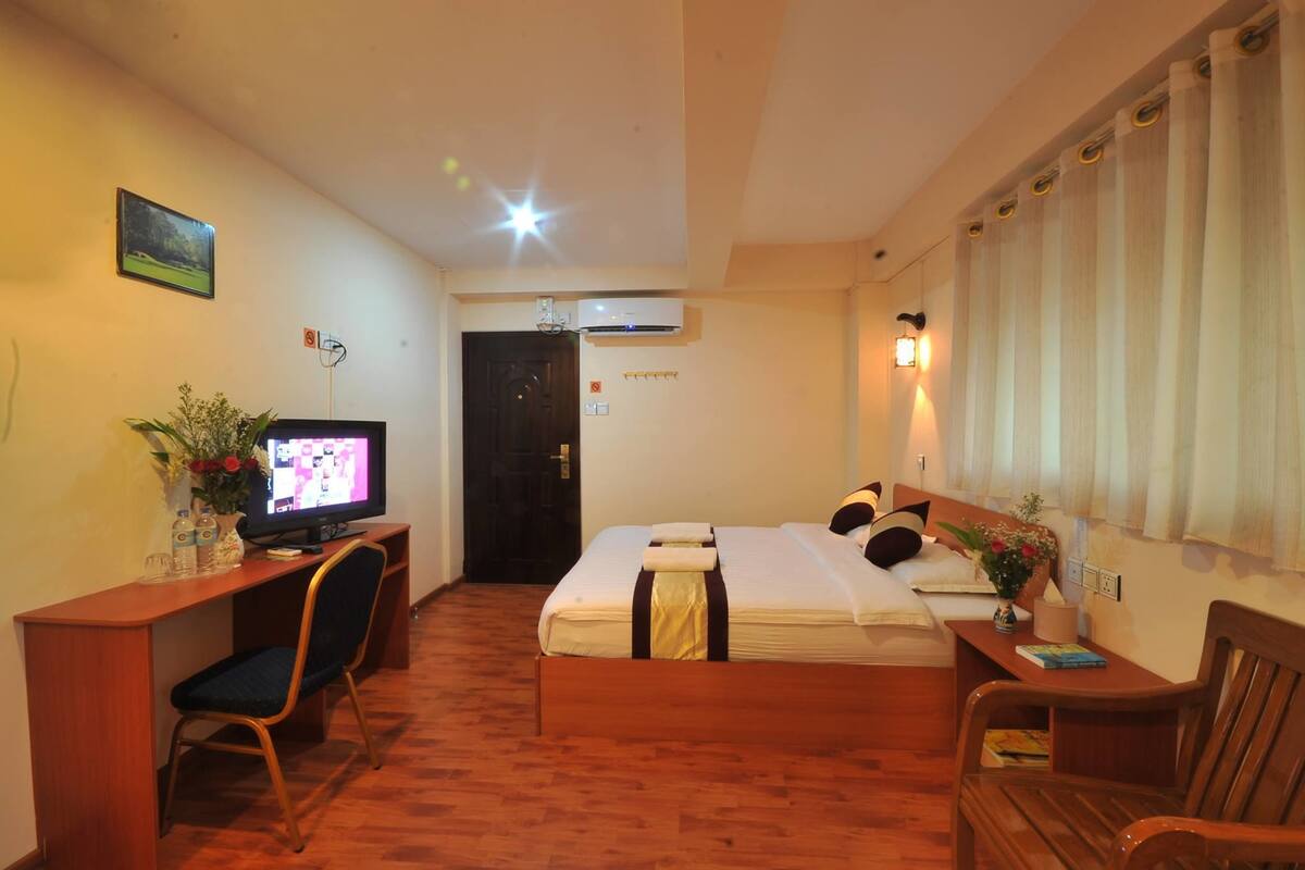 A hotel room with a bed, desk, chair, television, and a window with curtains.