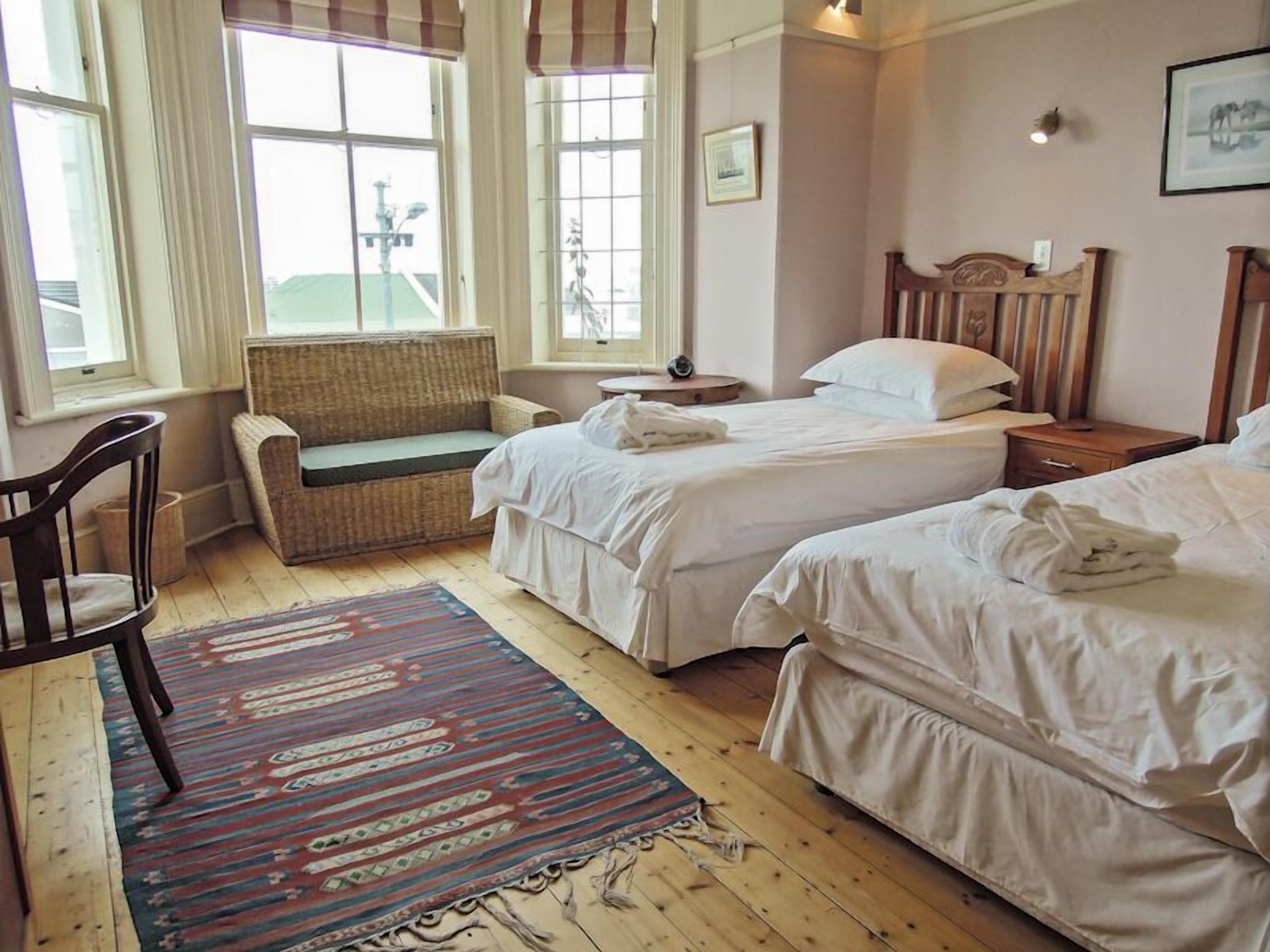 A hotel room with two beds, a wicker sofa, a patterned rug, and a wooden floor.
