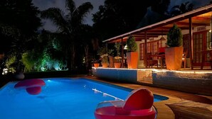 A swimming pool with a lounge area, surrounded by palm trees and a building with a covered patio. - Khashamongo B&B (Cape Town)