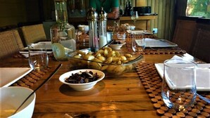 A dining table set with various dishes, including a bowl of potatoes and a bowl of olives. There are also several bottles and glasses on the table. - Khashamongo B&B (Cape Town)