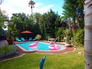Piscina com boias infláveis, cercada por um deck de madeira e uma área gramada.