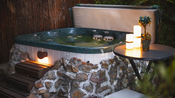 A hot tub with a stone wall, wooden steps, and a table with candles and a plant. - Khashamongo B&B (Cape Town)