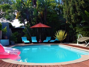 Piscina com cadeiras de descanso azuis e um guarda-sol vermelho.