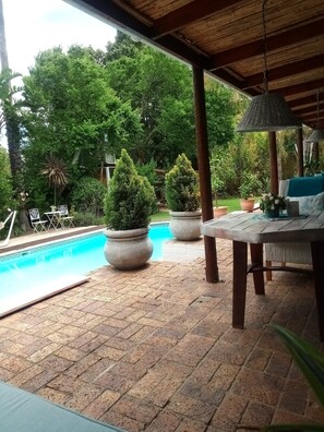 Área externa coberta com piscina, plantas em vasos e uma mesa com cadeiras.