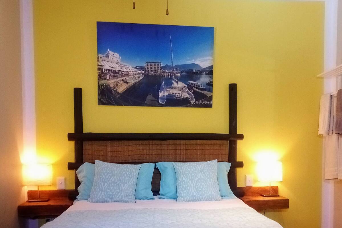 A bedroom with a bed, two bedside lamps, a ceiling fan, and a wall-mounted painting.