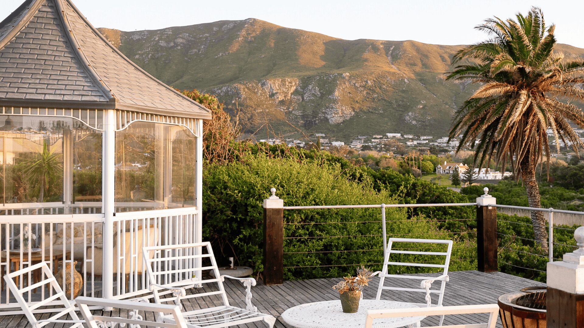 A gazebo with a glass enclosure, white outdoor furniture, and a view of a mountainous landscape.