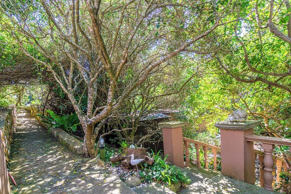 Un sendero de piedra que atraviesa un jardín exuberante con una valla de madera y un pequeño puente.