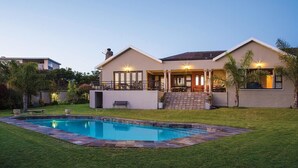 Ein modernes Haus mit Swimmingpool, überdachter Terrasse und gepflegtem Rasen.