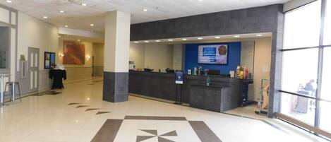 A reception area with a check-in counter, a large window, and a tiled floor with a geometric pattern.