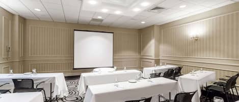 A conference room with multiple tables and chairs, a projector screen, and a carpeted floor.
