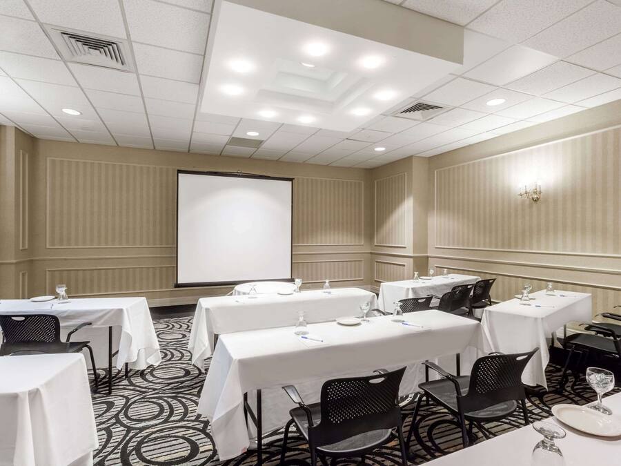 A conference room with multiple tables and chairs, a projector screen, and a carpeted floor.