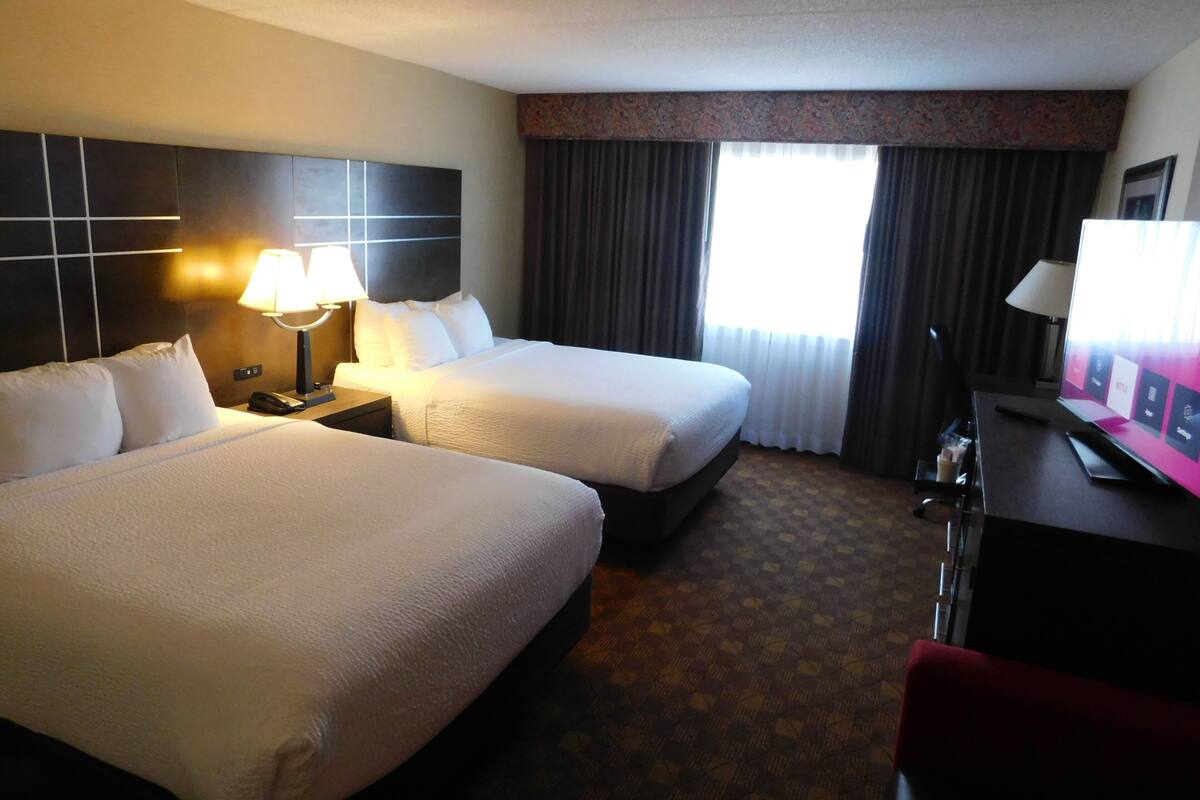Habitación de hotel con dos camas, un escritorio con computadora, una lámpara y una ventana con cortinas.