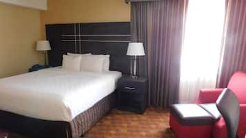 A hotel room with a large bed, bedside lamps, a red chair, and a patterned carpet.