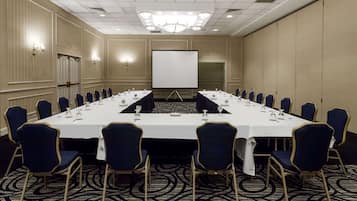 A conference room with a long table, blue chairs, a projector screen, and a chandelier.