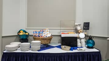 Una mesa de buffet con platos apilados, un bol de fruta, cajas de cereales y un cartel que indica una estación de café.