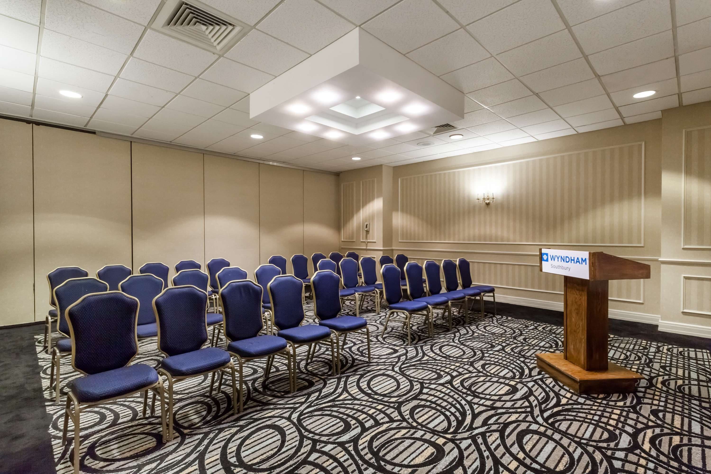 A conference room with rows of blue chairs, a podium, and a patterned carpet.