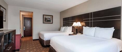 A hotel room with two beds, a desk, a TV, and a framed picture on the wall.