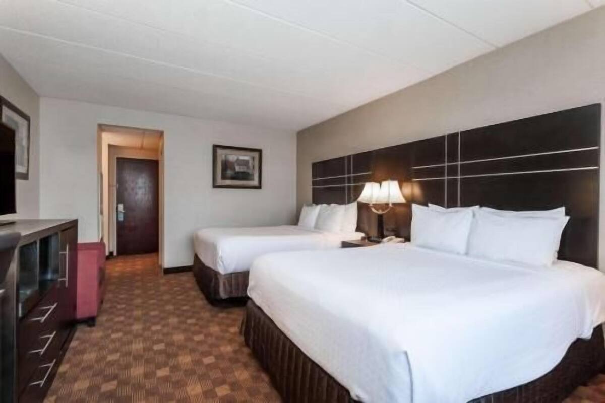 Una habitación de hotel con dos camas, un escritorio, una lámpara y un cuadro en la pared.