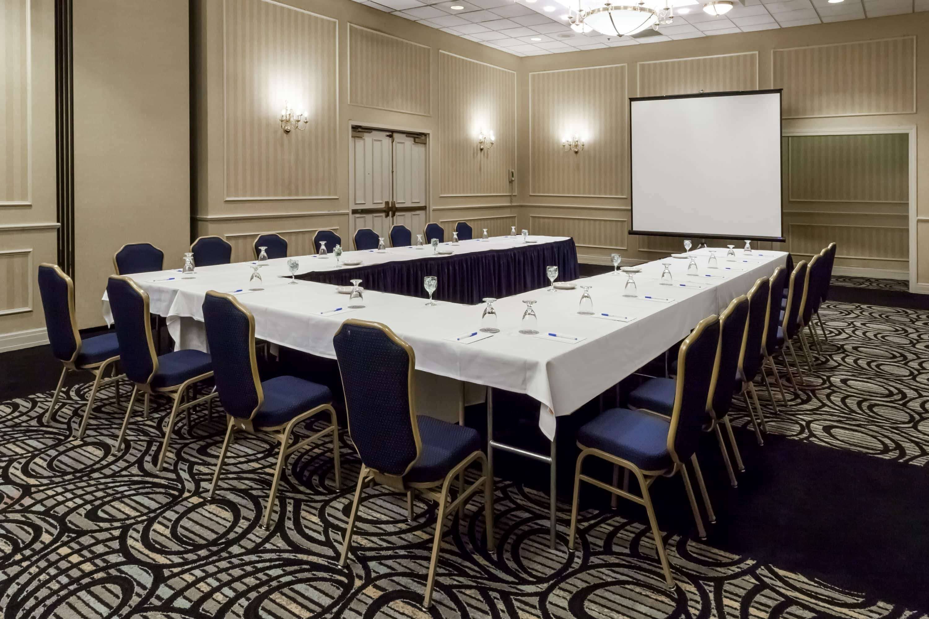 A conference room with a long table, chairs, a projector screen, and a carpeted floor.