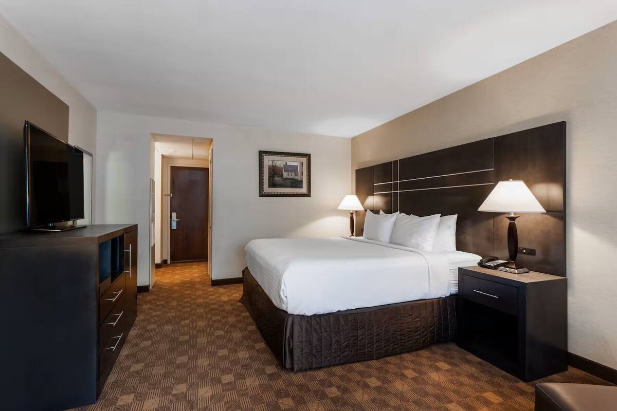 Una habitación de hotel con cama, lámparas de noche, televisión y escritorio con cajones.