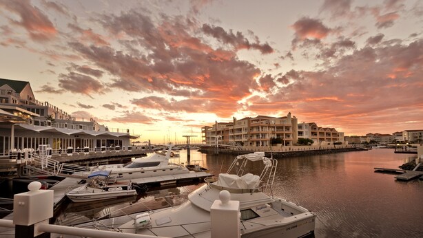 A marina with boats docked, a bridge, and buildings with balconies. - Krystal Beach Hotel (Cape Town)
