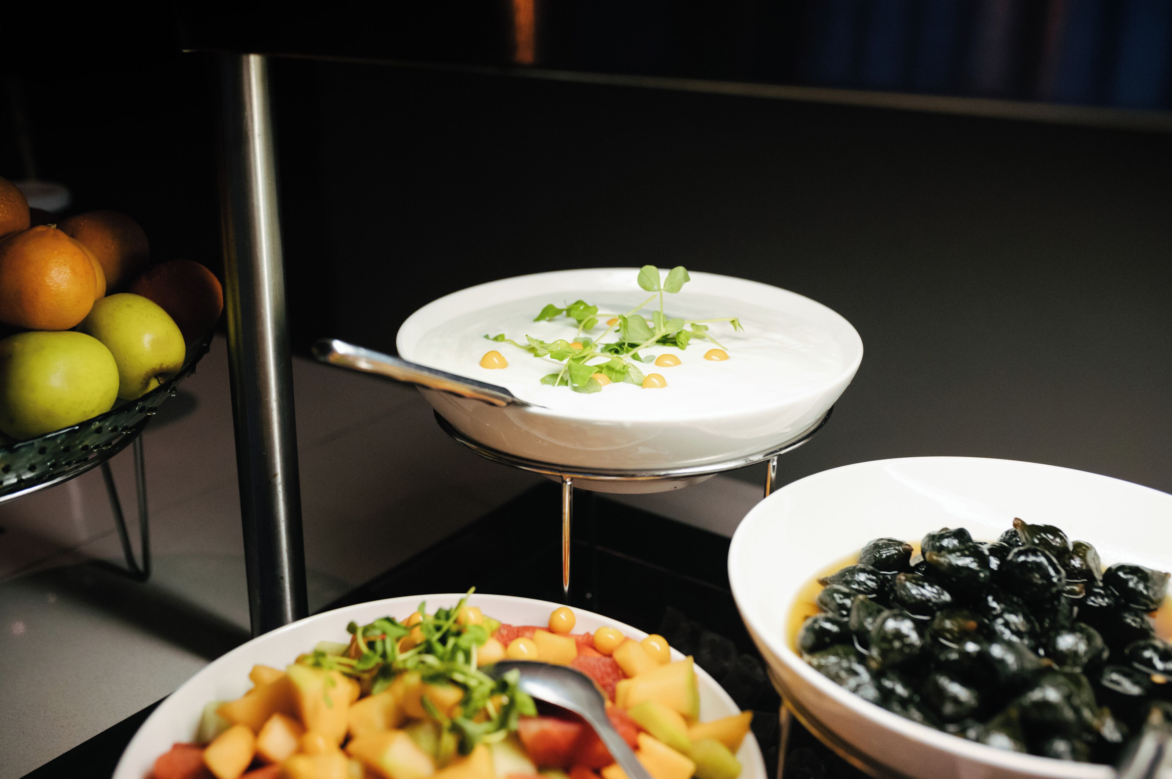 Una mesa de buffet con diversos platos, incluyendo frutas, verduras y un bol de aceitunas negras.
