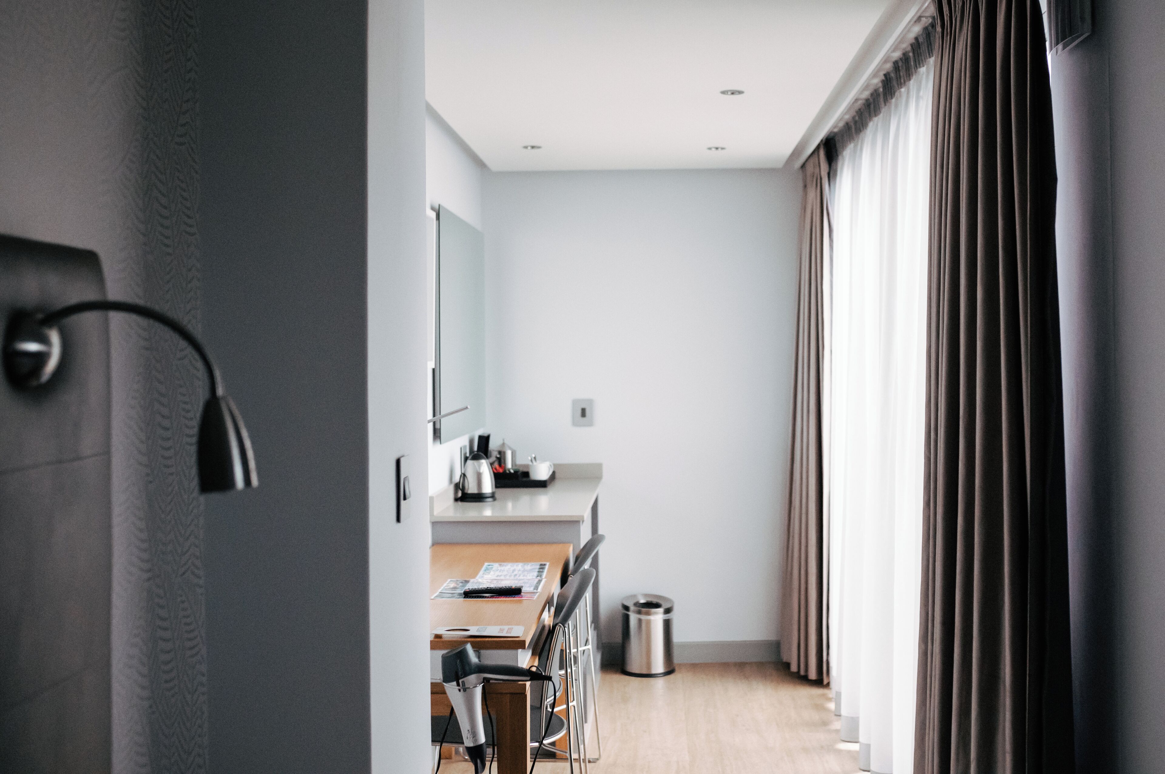 Et moderne hotelværelse med et tekøkken, spiseplads og et stort vindue med gardiner.