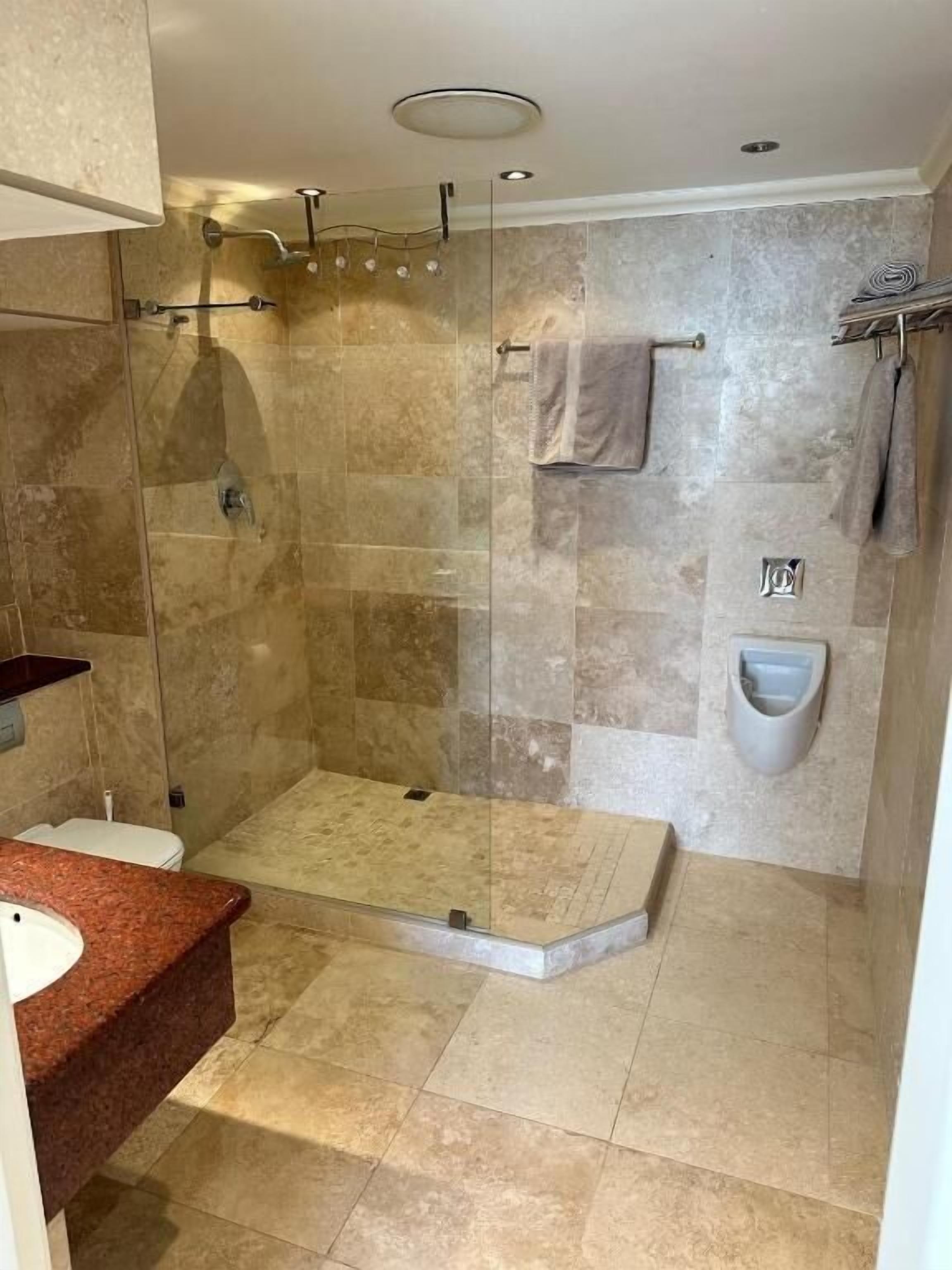 Un baño moderno con ducha de vidrio, suelo de mármol, lavabo empotrado y retrete.