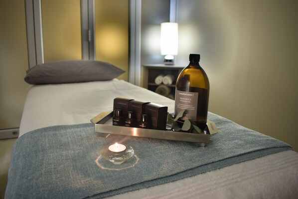 A neatly made bed with a tray of chocolates and a bottle of perfume on a blue towel. - Krystal Beach Hotel (Cape Town)
