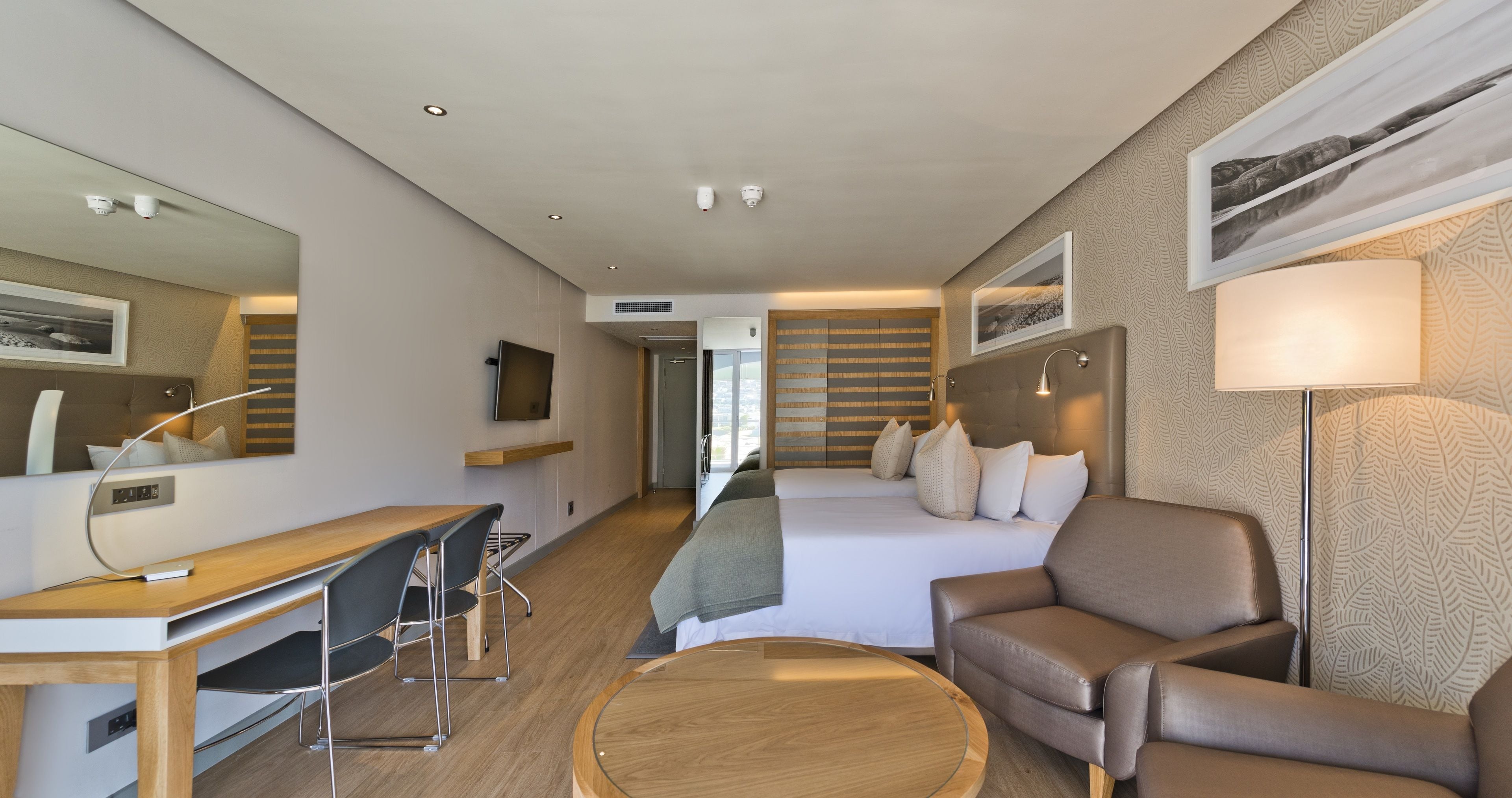 Ein modernes Hotelzimmer mit einem Holzbüro, einer bequemen Couch, einem Bett mit Kopfteil und einem großen Spiegel.