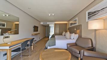 A modern hotel room with a wooden desk, a comfortable sofa, a bed with a headboard, and a large mirror.