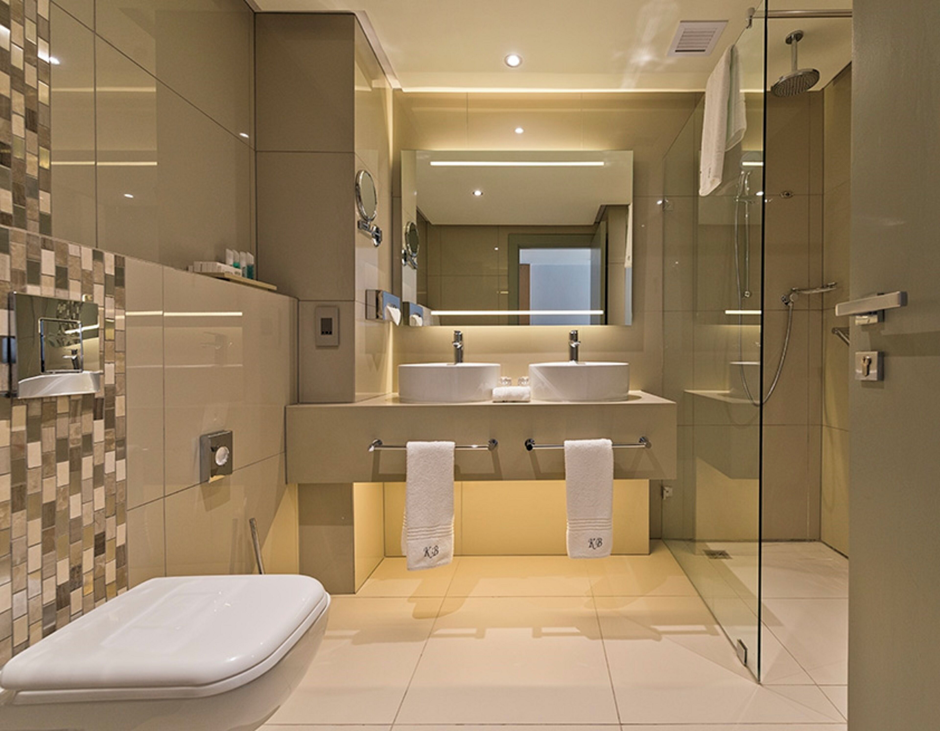 Un baño moderno con cabina de ducha de vidrio, dos lavamanos y un inodoro.